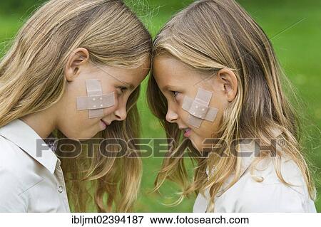 "Twin girls, 9, standing forehead to forehead, with plaster strips on their cheeks" View Large Photo Image Stock Photo - "Twin girls, 9, standing forehead to forehead, with plaster strips on their cheeks". Fotosearch