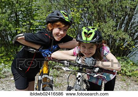 Stock Photograph - Two children, boy and girl with mountain bikes and helmets. Fotosearch