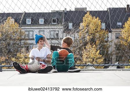 Two cool boys sitting with a basketball on a playground View Large Photo Image Stock Image - Two cool boys sitting with a basketball on a playground. Fotosearch