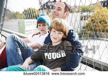 Two cool boys sitting with their father on a playground View Large Photo Image Stock Photograph - Two cool boys sitting with their father on a playground. Fotosearch