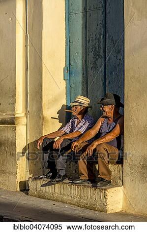 "Two elderly Cubans sitting on a doorstep in the evening light, smoking cigars, Trinidad, Sancti Spiritus Province, Cuba, North America" View Large Photo Image Stock Photography - "Two elderly Cubans sitting on a doorstep in the evening light, smoking cigars, Trinidad, Sancti Spiritus Province, Cuba, North America". Fotosearch