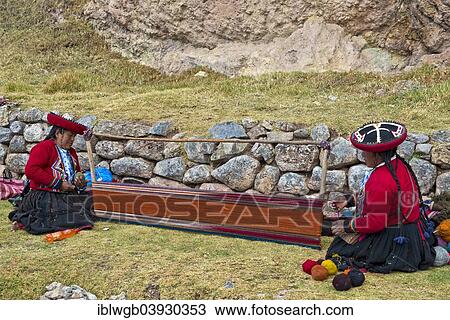 Stock Image - "Two elderly women wearing hats, Quechua Indians in traditional dress, squatting on the floor working on the stretcher of a loom, Cinchero, Urubamba Valley, Peru, South America". Fotosearch