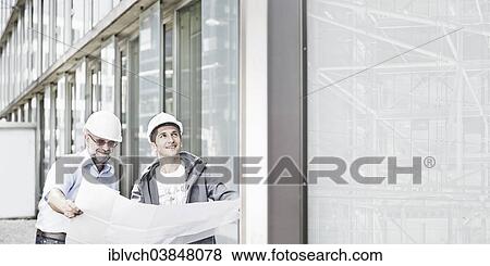 "Two engineers, 55-65 and 25-35 years old, wearing hard hats, standing in front of a building and looking at a building plan, Innsbruck, Tyrol, Austria, Europe" View Large Photo Image Stock Photo - "Two engineers, 55-65 and 25-35 years old, wearing hard hats, standing in front of a building and looking at a building plan, Innsbruck, Tyrol, Austria, Europe". Fotosearch