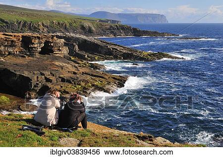 Stock Photograph - "Two female tourists on the lookout with binoculars, Yesnaby, Mainland, Orkney, Scotland, United Kingdom, Europe". Fotosearch