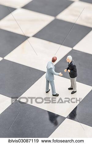 Stock Photo - Two figurines of businessmen standing on a chessboard shaking hands. Fotosearch