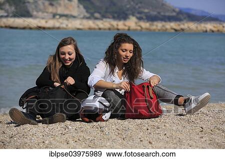 "Two girlfriends, teenagers, sitting on the beach with bags and a helmet, Menton, Alpes-Maritimes, Provence Alpes, France, Europe" View Large Photo Image Stock Photo - "Two girlfriends, teenagers, sitting on the beach with bags and a helmet, Menton, Alpes-Maritimes, Provence Alpes, France, Europe". Fotosearch