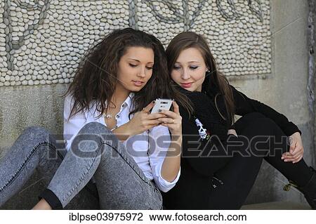 "Two girlfriends, teenagers, sitting back to back on a stone bench and reading a text message on a mobile phone, Menton, Provence-Alpes-Cote d'Azur, France, Europe" View Large Photo Image Stock Image - "Two girlfriends, teenagers, sitting back to back on a stone bench and reading a text message on a mobile phone, Menton, Provence-Alpes-Cote d'Azur, France, Europe". Fotosearch