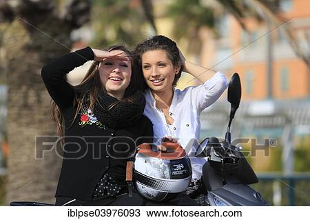 Stock Image - "Two girlfriends, teenagers, with a scooter, Menton, Alpes-Maritimes, Provence-Alpes-Cote d'Azur, France, Europe". Fotosearch