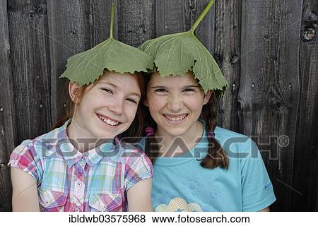 Stock Photo - "Two girls, 11 years, with leaves on their heads, coltsfoot leaves (Tussilago coltsfoot), natural sunshades". Fotosearch
