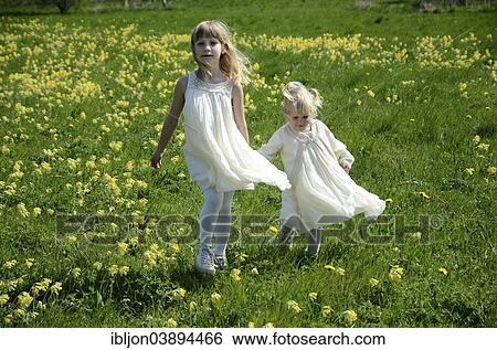 Stock Photograph - "Two girls, 7 and 2 years, wearing summer dresses, in a field of cowslip, Sweden, Europe". Fotosearch