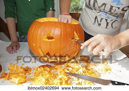 Picture - "Two girls, about 14 years, carving a face into a Halloween pumpkin". Fotosearch
