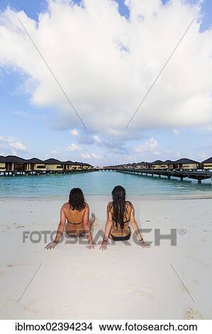 Picture - "Two girls, about 15 and 19 years old sitting on the beach, lagoon, Paradise Island at the back, Lankanfinolhu, North Male Atoll, Republic of Maldives, Indian Ocean, Asia". Fotosearch