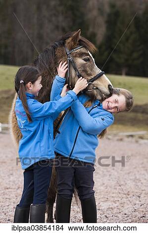 "Two girls standing beside a pony, dun, with a bridle, Tyrol, Austria, Europe" View Large Photo Image Picture - "Two girls standing beside a pony, dun, with a bridle, Tyrol, Austria, Europe". Fotosearch