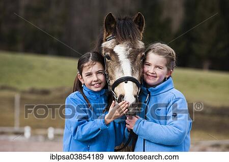 "Two girls standing beside a pony, dun, with a bridle, Tyrol, Austria, Europe" View Large Photo Image Stock Photo - "Two girls standing beside a pony, dun, with a bridle, Tyrol, Austria, Europe". Fotosearch