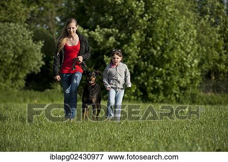 Two girls walking with a Doberman across a meadow View Large Photo Image Stock Photo - Two girls walking with a Doberman across a meadow. Fotosearch