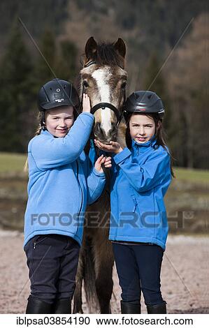 "Two girls wearing riding helmets standing beside a pony, dun, with a bridle, Tyrol, Austria, Europe" View Large Photo Image Stock Image - "Two girls wearing riding helmets standing beside a pony, dun, with a bridle, Tyrol, Austria, Europe". Fotosearch