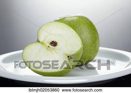 Stock Image - "Two green Granny Smith apples, one cut open, on a white plate". Fotosearch