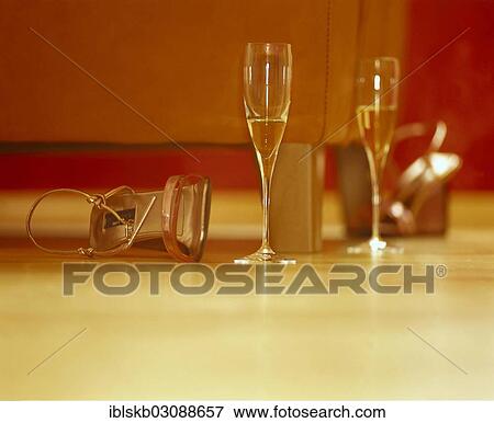 Stock Photo - Two half-full glasses of champagne on the floor in front of the sofa beside a pair of women's shoes. Fotosearch
