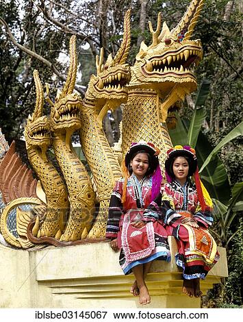 Stock Photo - "Two Lisu hill tribe girls wearing traditional costumes and headdresses sitting on a Naga sculpture, Buddhist temple, Mae Sai, Chiang Rai Province, Northern Thailand, Thailand, Asia". Fotosearch