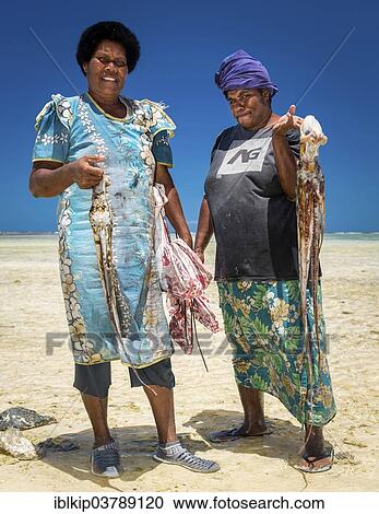 Stock Image - "Two local women returning with their catch of octopus, Viti Levu, Fiji, Oceania". Fotosearch
