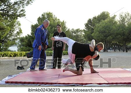 Two men doing martial arts on a mat in a park being watched by a trainer and his student View Large Photo Image Stock Image - Two men doing martial arts on a mat in a park being watched by a trainer and his student. Fotosearch