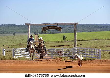 Stock Photography - "Two men riding horses, cowboys, entrance of a fazenda or ranch of a landowner, Campito, Caaguazu Department, Paraguay, South America". Fotosearch