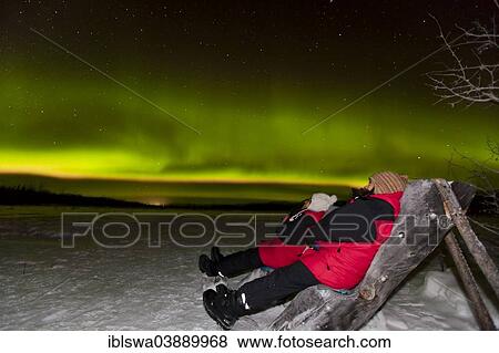 Stock Photo - "Two people sitting in a wooden chair, watching northern polar lights, near Whitehorse, Yukon Territory, Canada, North America". Fotosearch
