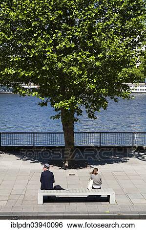 "Two people sitting on concrete bench by river with tree, London, England, United Kingdom, Europe" View Large Photo Image Stock Photograph - "Two people sitting on concrete bench by river with tree, London, England, United Kingdom, Europe". Fotosearch