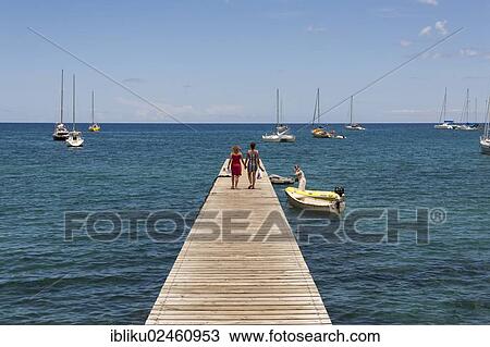 Stock Image - "Two people walking on a jetty, Deshaies, Guadeloupe, Lesser Antilles, Caribbean, North America". Fotosearch
