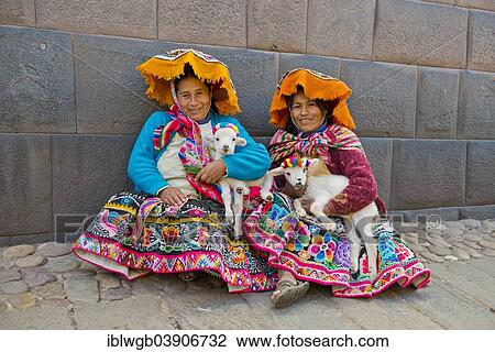 Stock Image - "Two Quechua women in traditional dress holding lambs in their arms, sitting on the ground, Cusco Province, Southern Peru, Peru, South America". Fotosearch