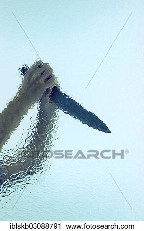 Stock Image - Two raised hands holding a large butcher's knife behind cathedral glass. Fotosearch
