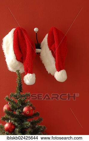 "Two Santa hats hanging on nostalgic coat hooks, Christmas tree at front" View Large Photo Image Picture - "Two Santa hats hanging on nostalgic coat hooks, Christmas tree at front". Fotosearch