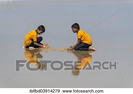 Stock Photo - "Two schoolboys wearing yellow shirts playing on the beach, reflection, Varkala, Kerala, India, Asia". Fotosearch