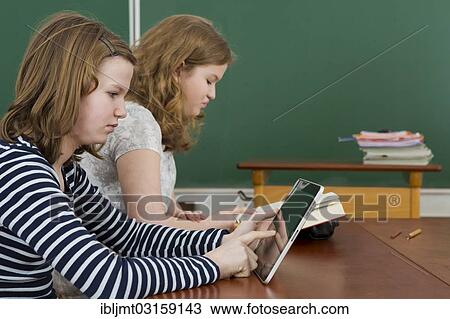 "Two schoolgirls in the classroom, one is reading a book, the other is using a tablet PC, Germany, Europe" View Large Photo Image Stock Image - "Two schoolgirls in the classroom, one is reading a book, the other is using a tablet PC, Germany, Europe". Fotosearch