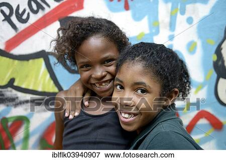 "Two smiling girls embracing each other in front of a graffiti-sprayed wall, slum, Mangueirinha favela, Duque de Caxias, Rio de Janeiro, Brazil, South America" View Large Photo Image Stock Photo - "Two smiling girls embracing each other in front of a graffiti-sprayed wall, slum, Mangueirinha favela, Duque de Caxias, Rio de Janeiro, Brazil, South America". Fotosearch