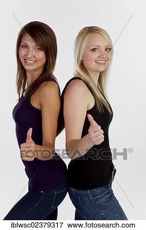 Stock Photo - Two smiling young women looking into the camera making thumbs up gesture. Fotosearch