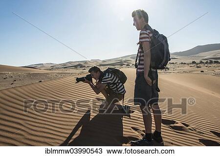 Stock Image - "Two teenagers standing on a dune, taking photos, Sossusvlei, Namib Desert, Hardap Region, Namibia, Africa". Fotosearch