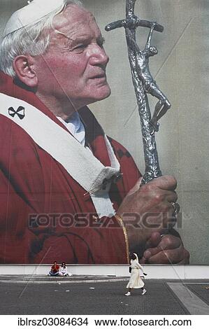 Picture - "Two tourists sitting in front of a huge poster of Pope John Paul II, nun walking in front of poster, Vatikanstadt, Italy, Europe". Fotosearch