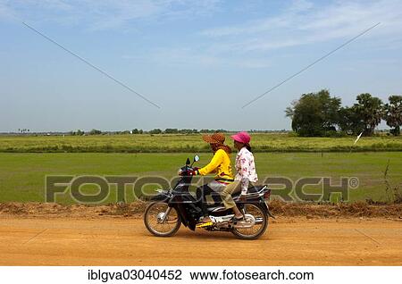 Stock Image - "Two women riding on a motorcycle on a country road, Cambodia, Asia". Fotosearch