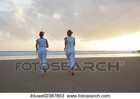 Stock Image - Two women running along the beach at sunset. Fotosearch