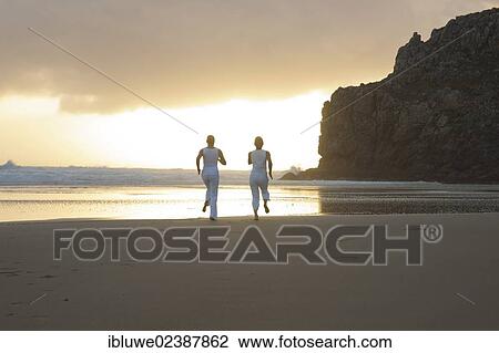 Stock Image - Two women running along the beach at sunset. Fotosearch