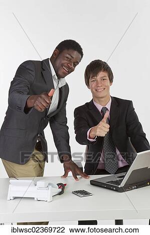Two young businessmen of different races with a laptop and making a thumbs-up gesture View Large Photo Image Stock Image - Two young businessmen of different races with a laptop and making a thumbs-up gesture. Fotosearch