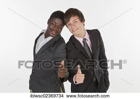 Two young businessmen standing back to back and making a thumbs-up gesture View Large Photo Image Picture - Two young businessmen standing back to back and making a thumbs-up gesture. Fotosearch