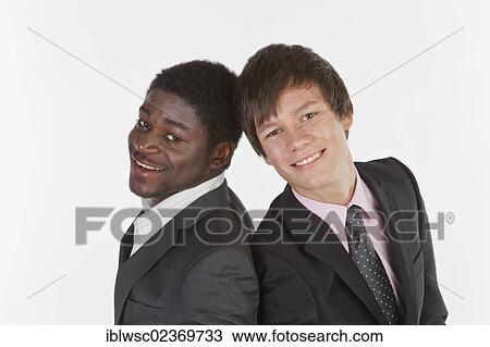 Two young businessmen standing back to back and smiling View Large Photo Image Stock Image - Two young businessmen standing back to back and smiling. Fotosearch