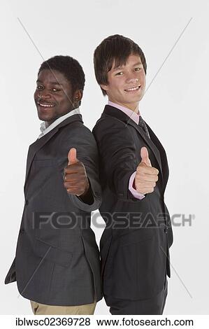 Two young businessmen standing back to back and making a thumbs-up gesture View Large Photo Image Stock Photo - Two young businessmen standing back to back and making a thumbs-up gesture. Fotosearch