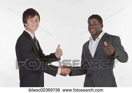 Two young men of different races shaking hands and making a thumbs-up gesture View Large Photo Image Stock Photograph - Two young men of different races shaking hands and making a thumbs-up gesture. Fotosearch