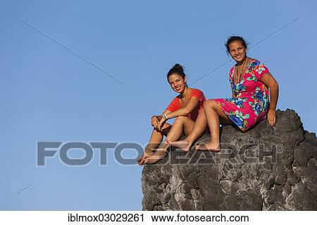 "Two young women, ca. 15 and 19, sitting on a rock in front of the blue sky, Sukadana, Tukad Batang, Bali, Indonesia, Asia" View Large Photo Image Stock Image - "Two young women, ca. 15 and 19, sitting on a rock in front of the blue sky, Sukadana, Tukad Batang, Bali, Indonesia, Asia". Fotosearch
