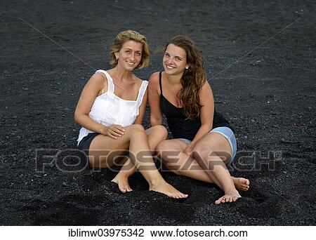 Stock Image - "Two young women, girlfriends, on a black lava beach, Lanzarote, Canary Islands, Spain, Europe". Fotosearch
