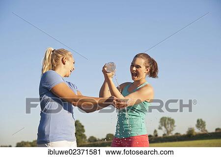 Two young women having fun with a bottle of water during a drink break while doing sports View Large Photo Image Stock Image - Two young women having fun with a bottle of water during a drink break while doing sports. Fotosearch