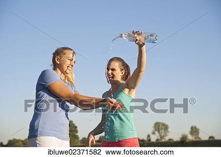 Two young women having fun with a bottle of water during a drink break while doing sports View Large Photo Image Stock Image - Two young women having fun with a bottle of water during a drink break while doing sports. Fotosearch